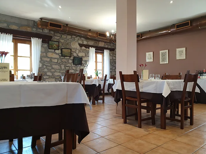 El comedor grande de Autzagane, con pared de piedra vista y mesas vestidas de blanco.