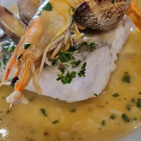 Merluza en salsa verde con almejas y un langostino encima.