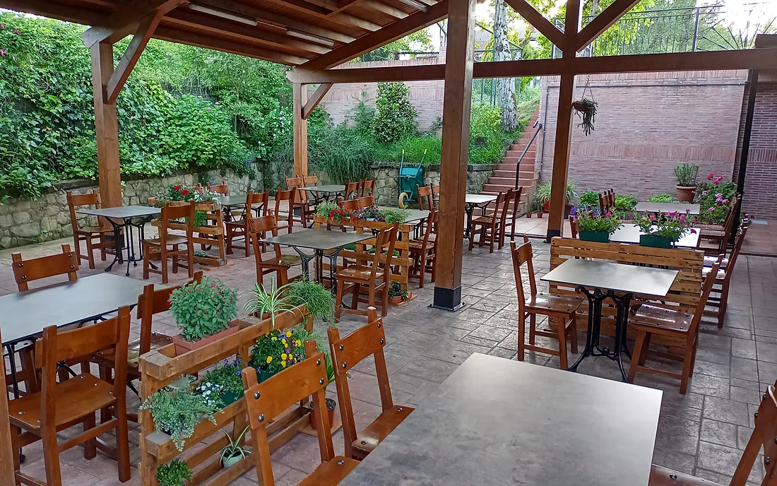 La terraza-comedor cubierta de Autzagane: mesas y sillas de madera bajo una pérgola, con el jardín detrás.